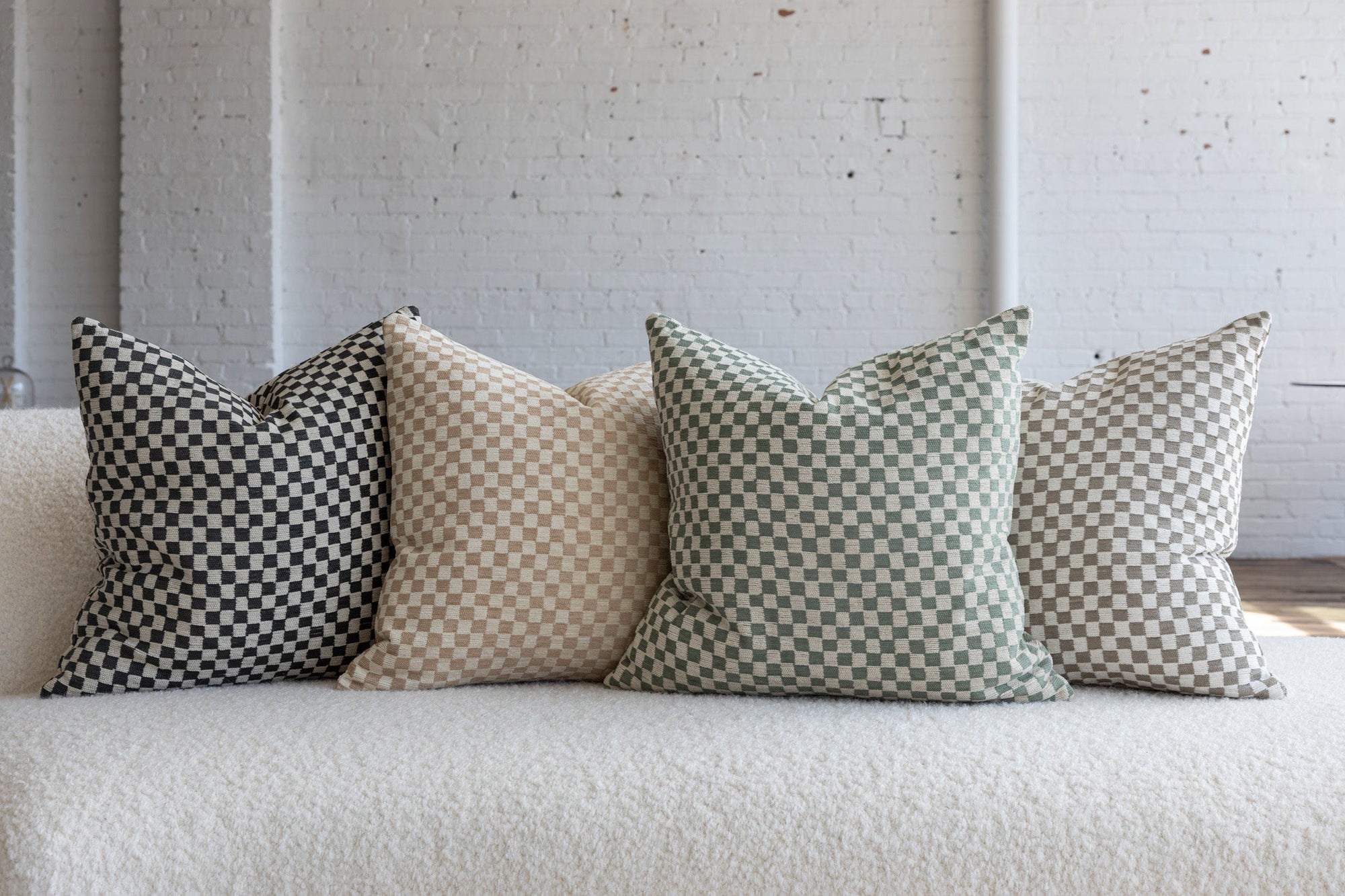 Olive green and cream checkerboard pillow with black, cream, and light gray variations on white boucle sofa