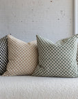 Light gray and cream checkerboard pillow with black, cream, and olive green variations on white boucle sofa