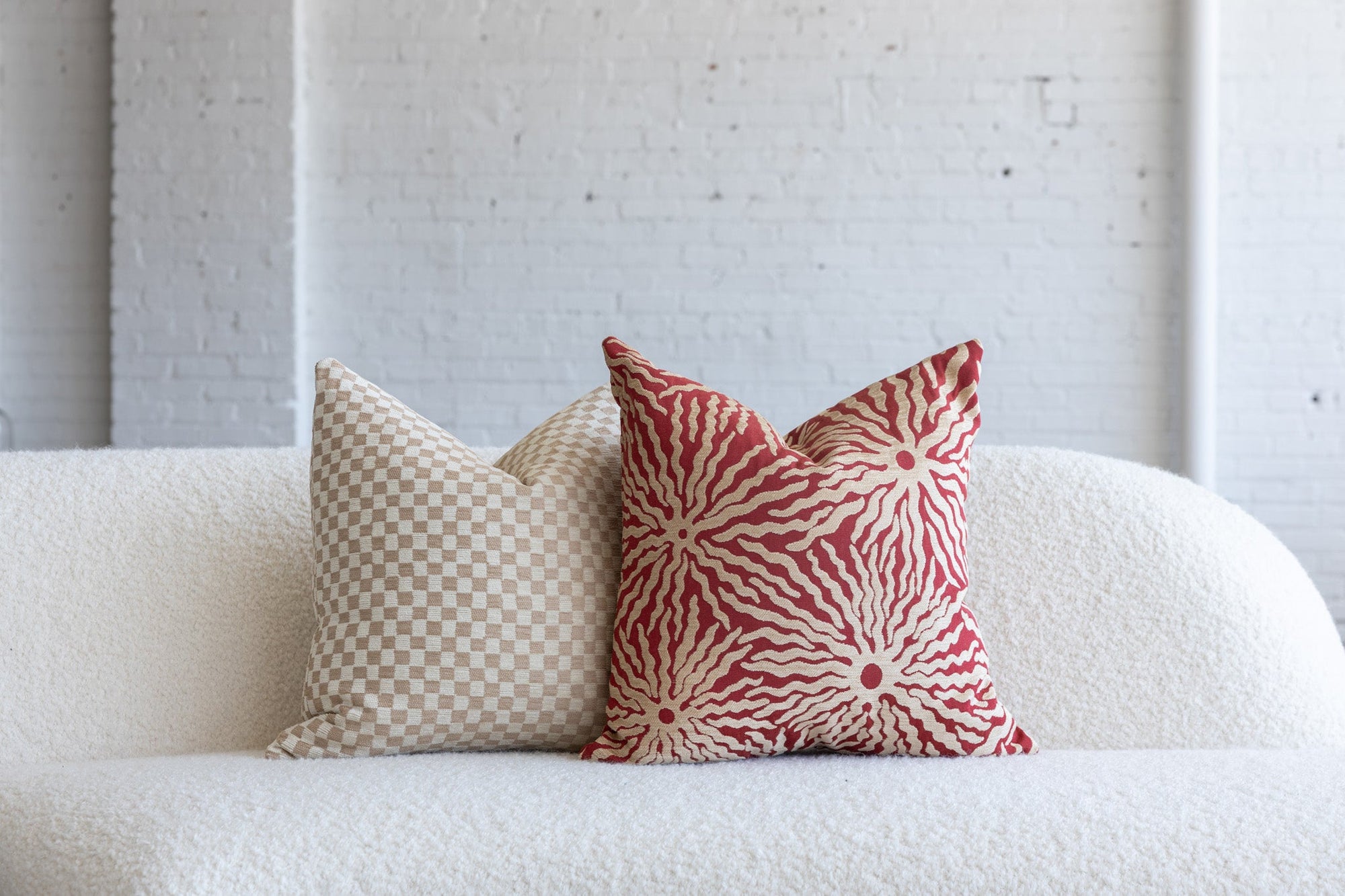 Red and cream sunburst pillow styled with cream checkerboard pillows on white boucle sofa