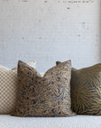 Dark brown with gold and blue botanical leaf pillow styled with cream checkerboard and gold sunburst pillows on white boucle sofa