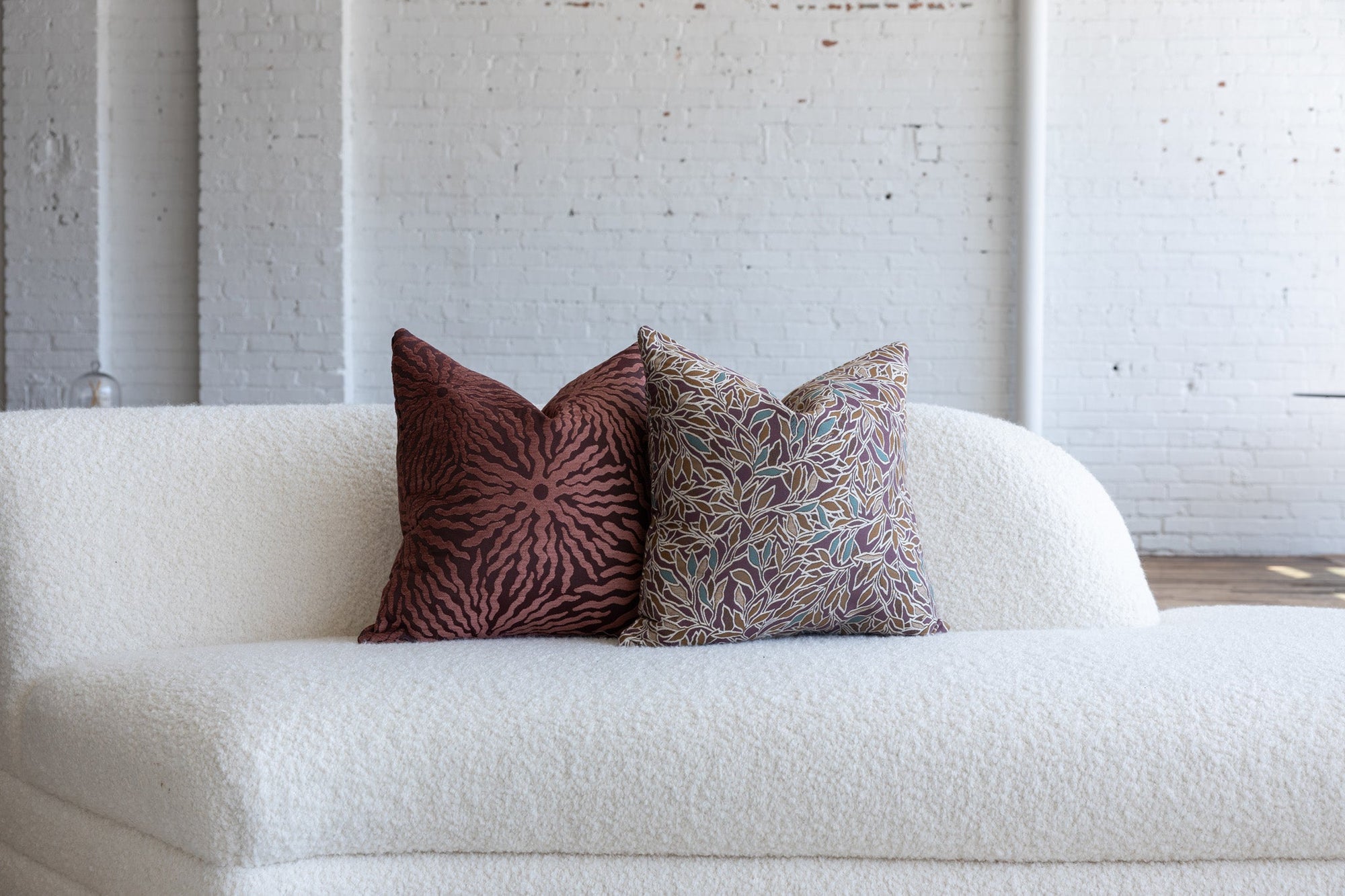 Deep maroon with teal botanical leaf pillow styled with maroon sunburst pillows on white boucle sofa