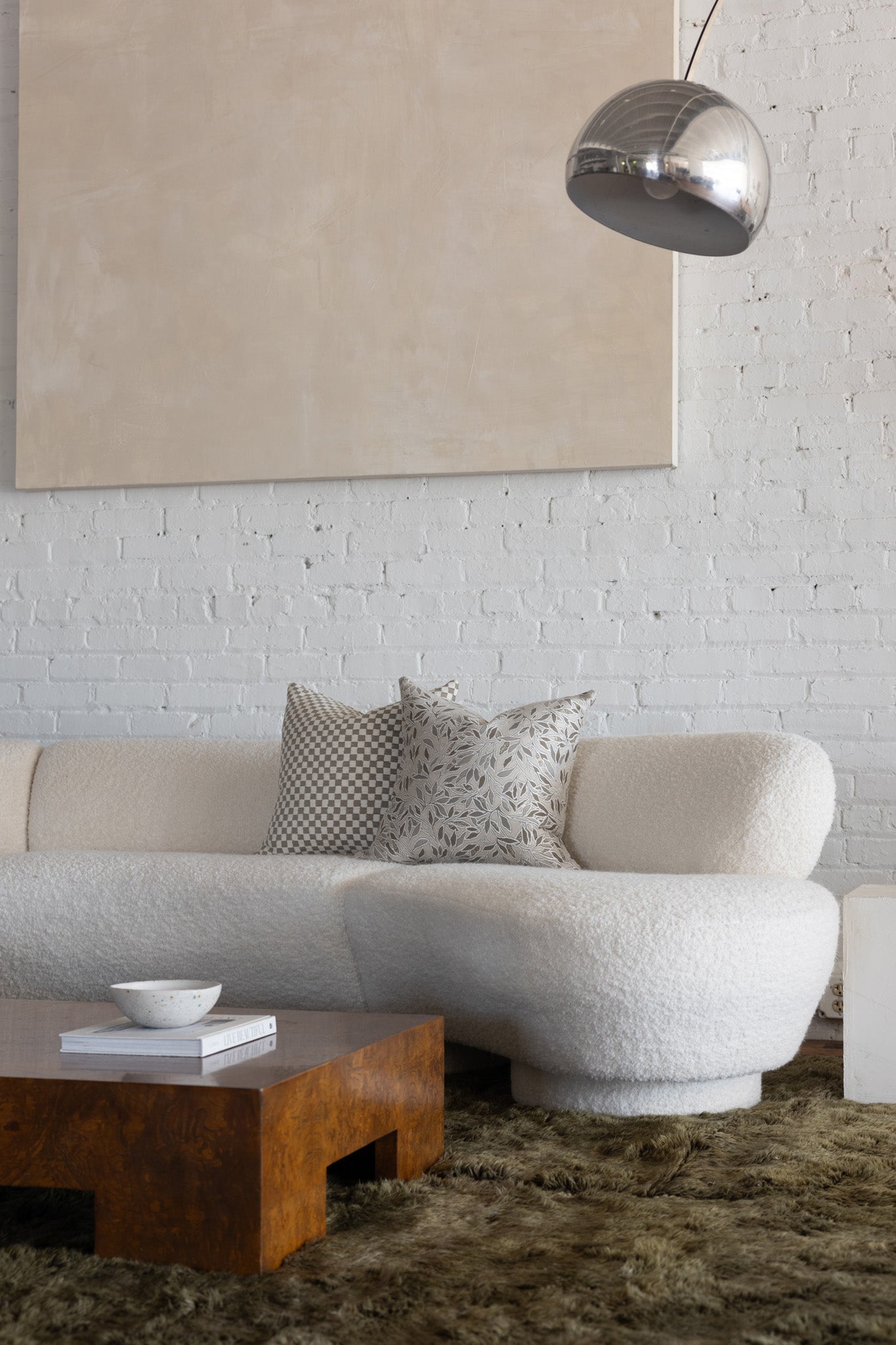 Cream and tan checkerboard pillow styled with cream botanical leaf pillows on white boucle sofa
