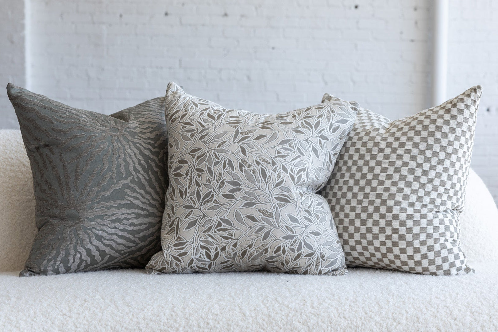 Cream and gray botanical leaf pillow styled with silver gray sunburst and cream checkerboard pillows on white boucle sofa