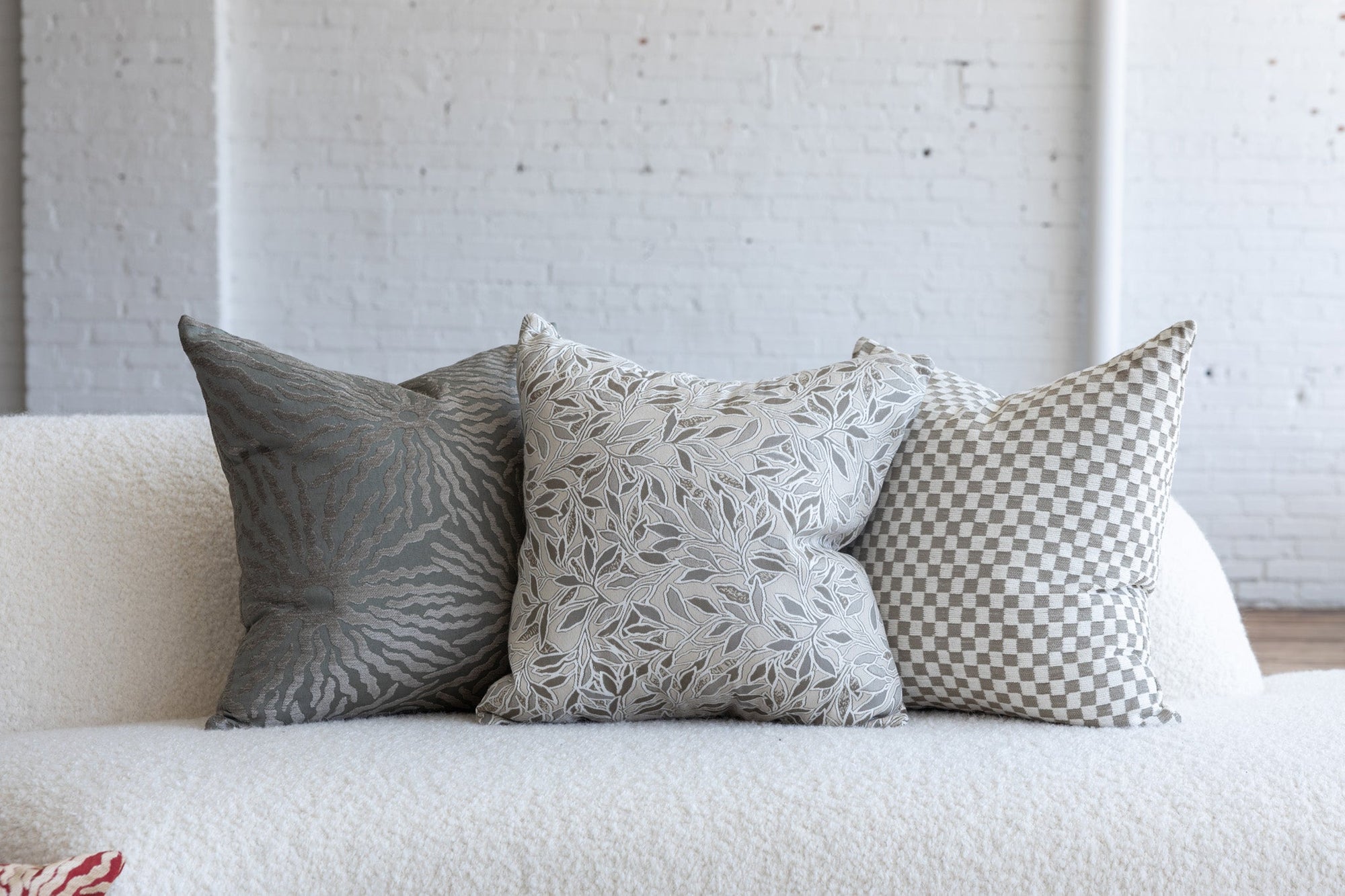 Silver gray sunburst pillow styled with cream botanical leaf and cream checkerboard pillows on white boucle sofa
