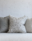 Cream and tan checkerboard pillow styled with silver gray sunburst and cream botanical leaf pillows on white boucle sofa
