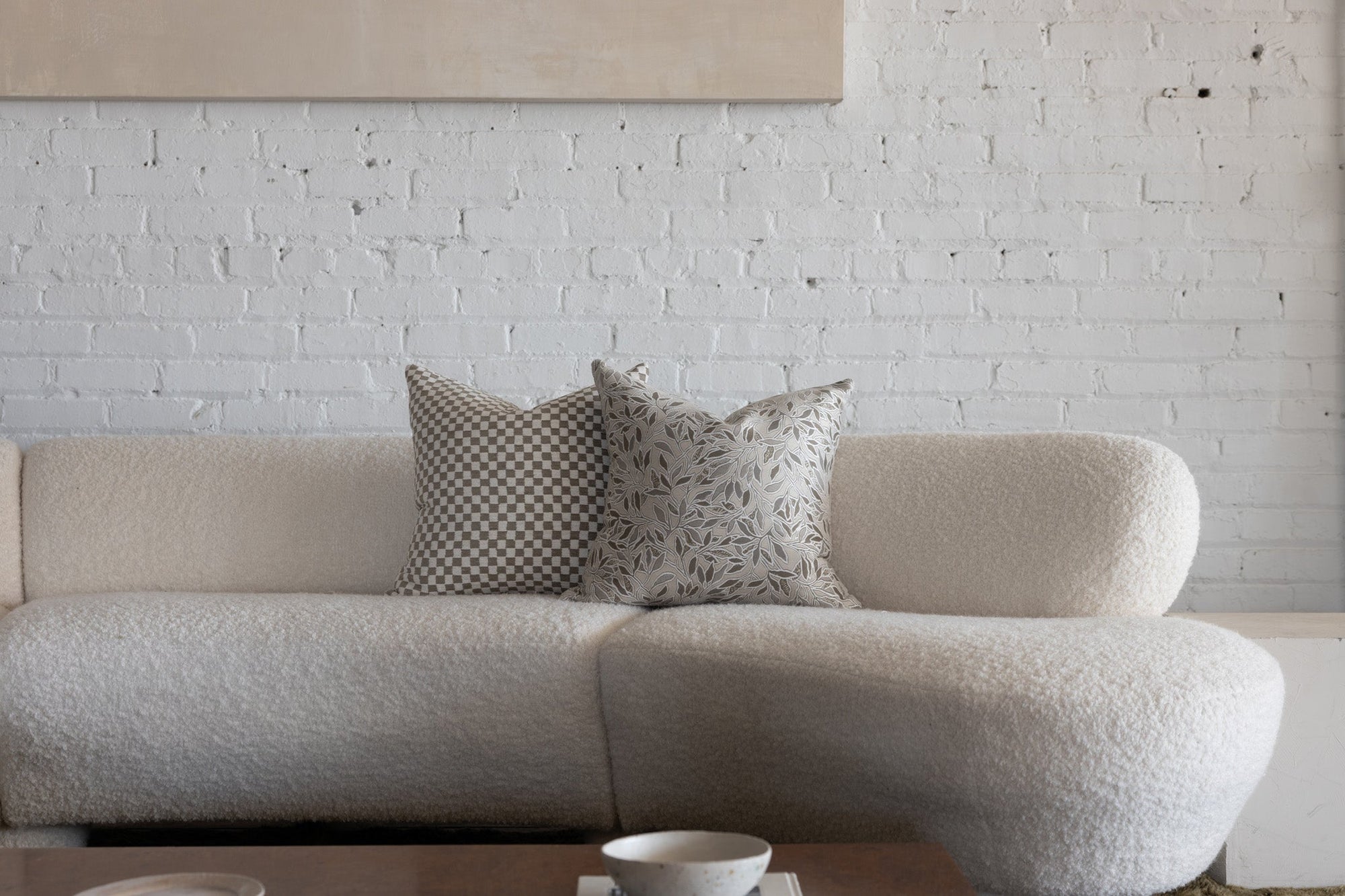 Cream and gray botanical leaf pillow styled with cream checkerboard pillows on white boucle sofa
