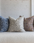Deep maroon with teal botanical leaf pillow with dark brown, blue, cream, and sage green variations on white boucle sofa