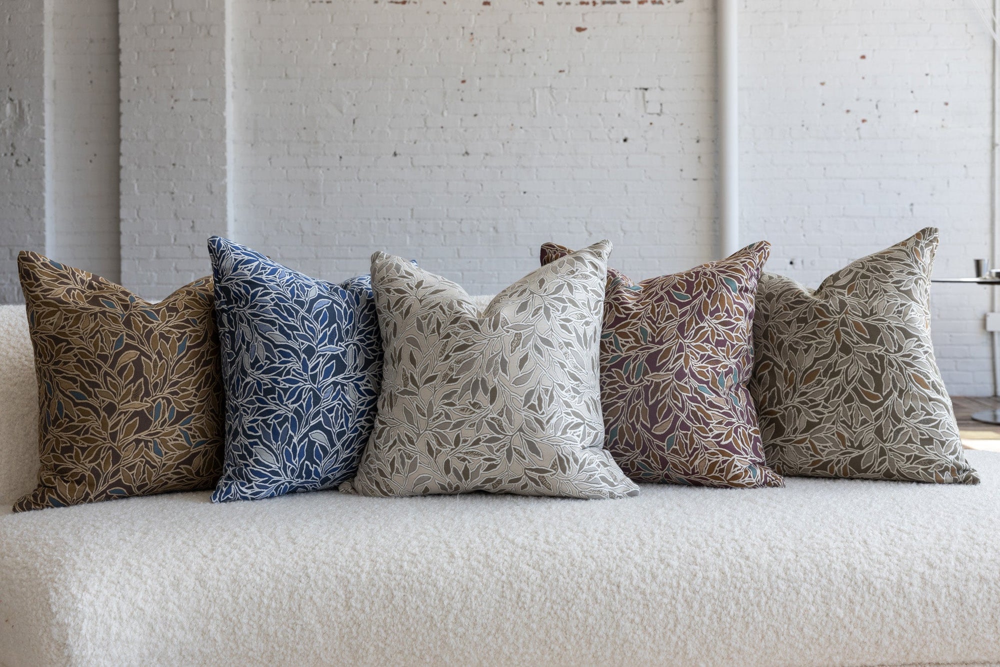 Blue and cream botanical leaf pillow with dark brown, cream, deep maroon, and sage green variations on white boucle sofa