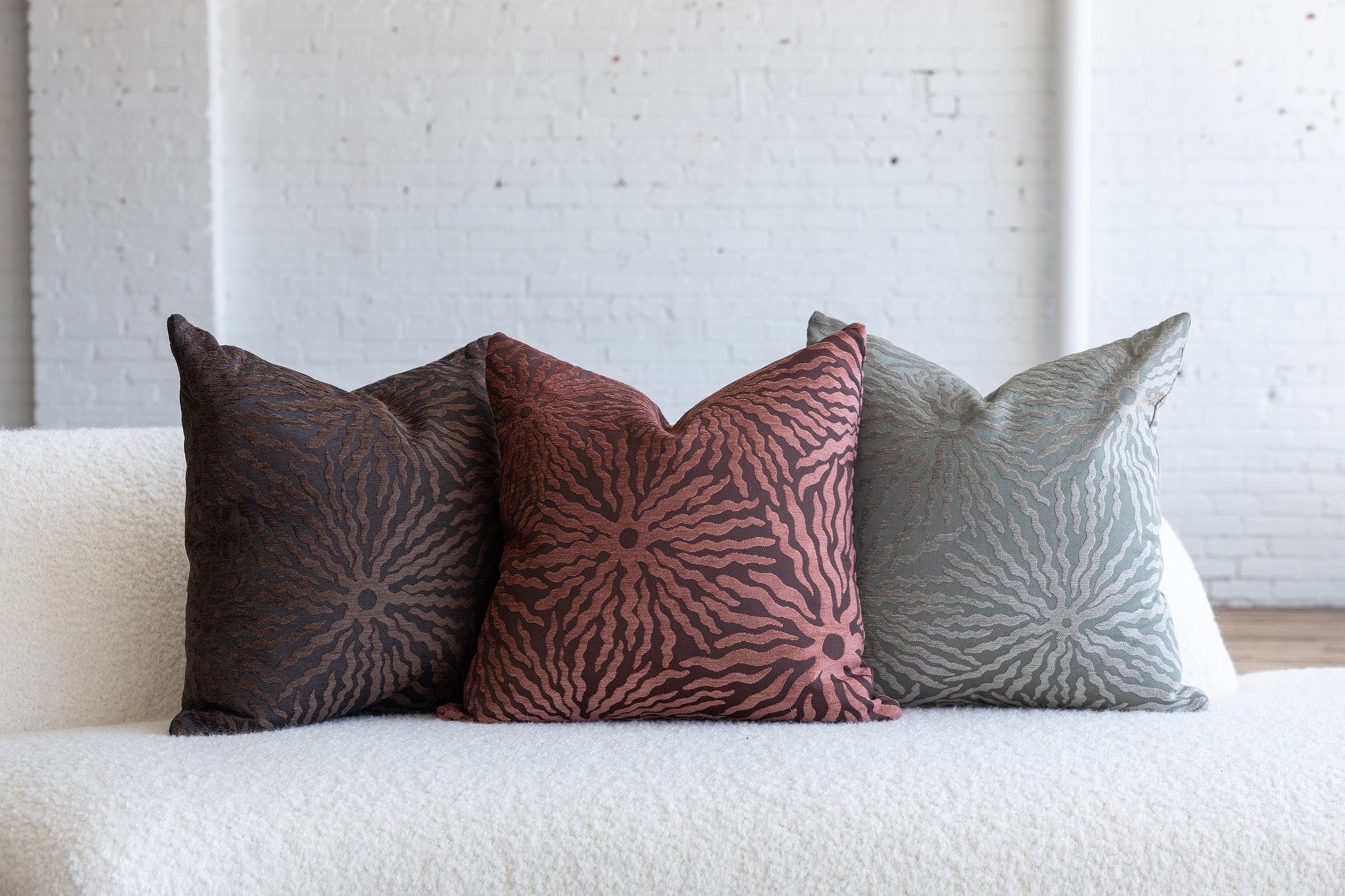 Maroon sunburst pillow with dark brown and silver gray variations on white boucle sofa