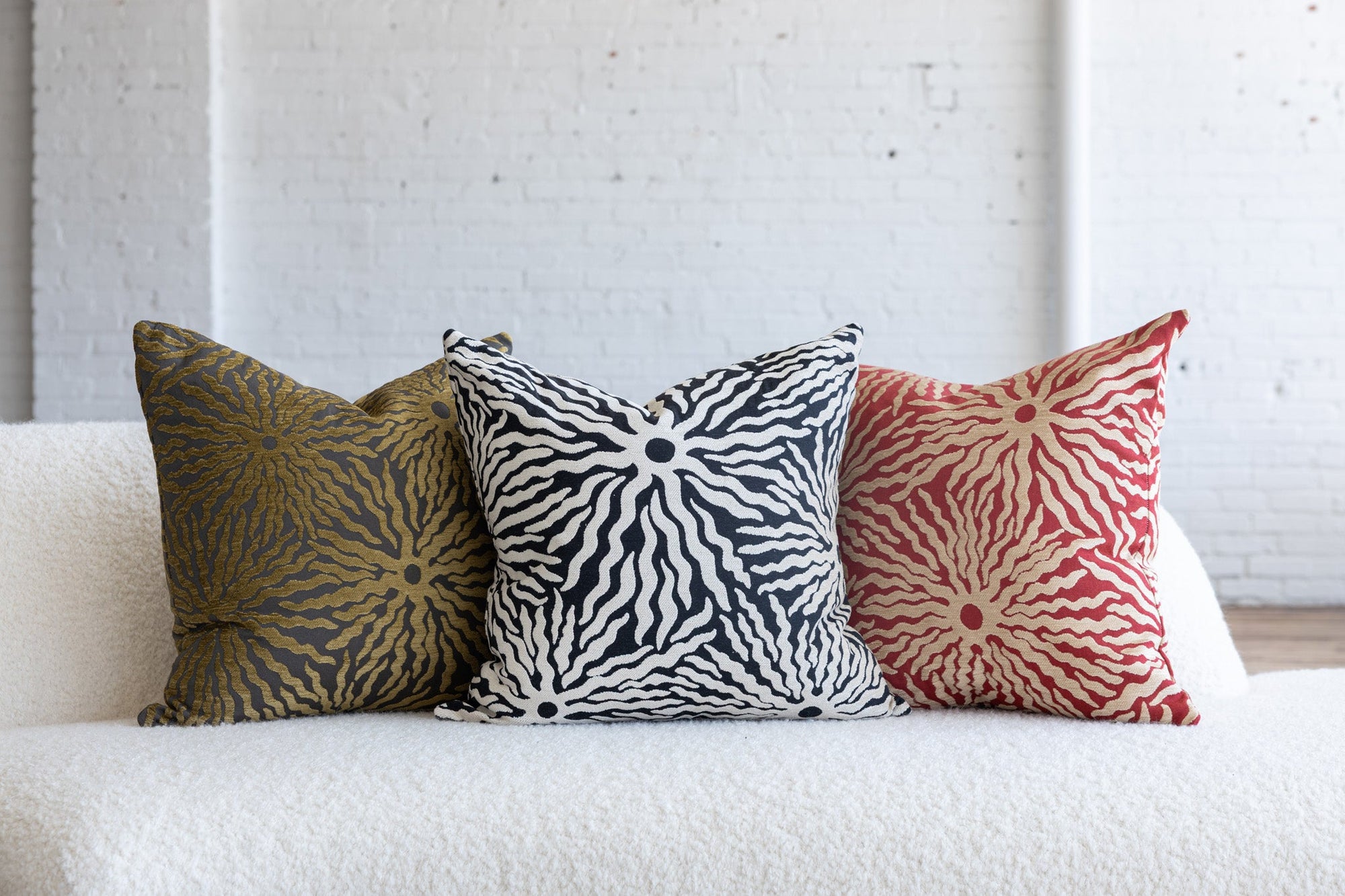 Black and ivory sunburst pillow with gold and red variations on white boucle sofa
