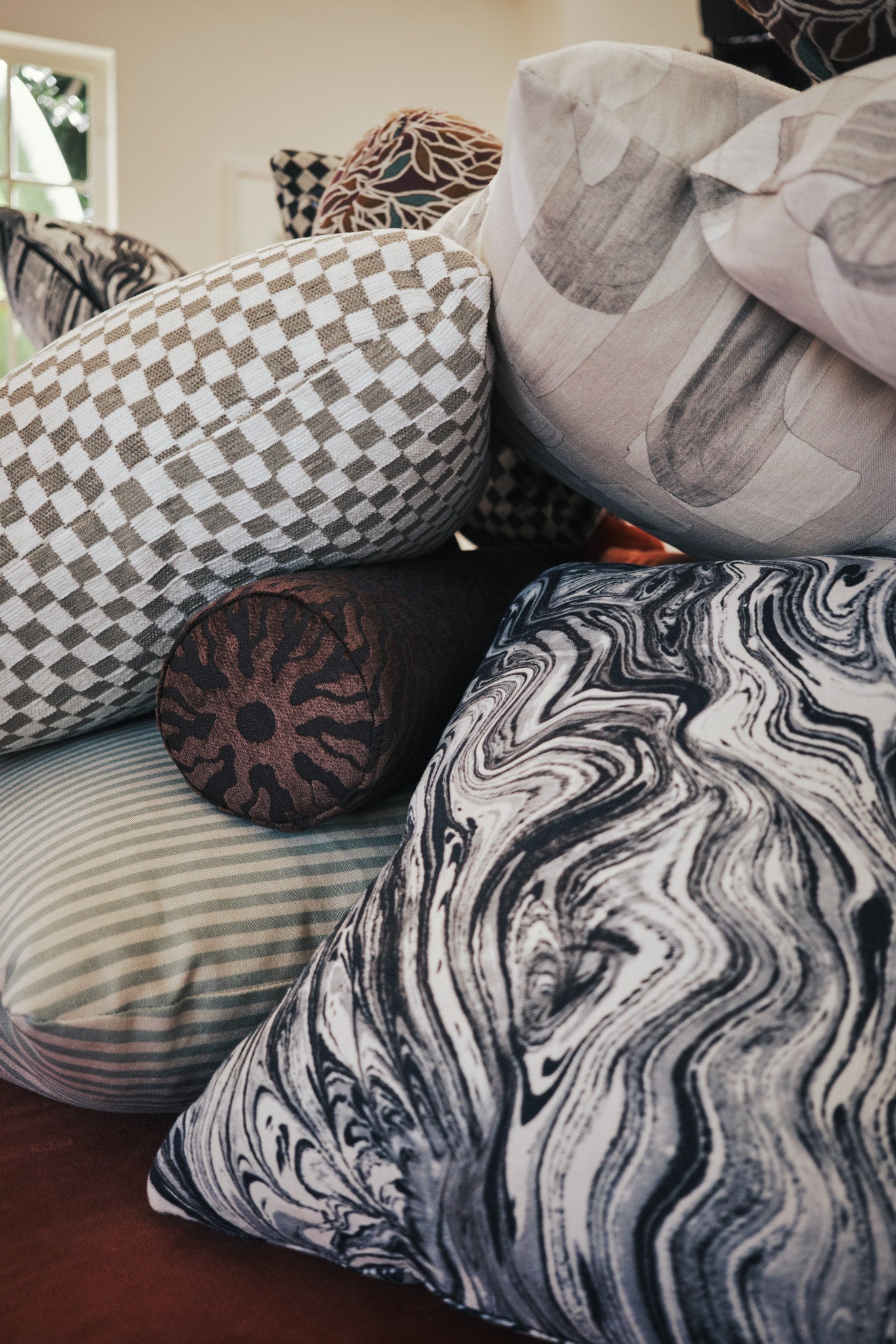 Gray checkerboard jacquard fabric made up as a throw pillow among a mix of patterned pillows in daylight