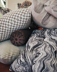 Gray checkerboard jacquard fabric made up as a throw pillow among a mix of patterned pillows in daylight