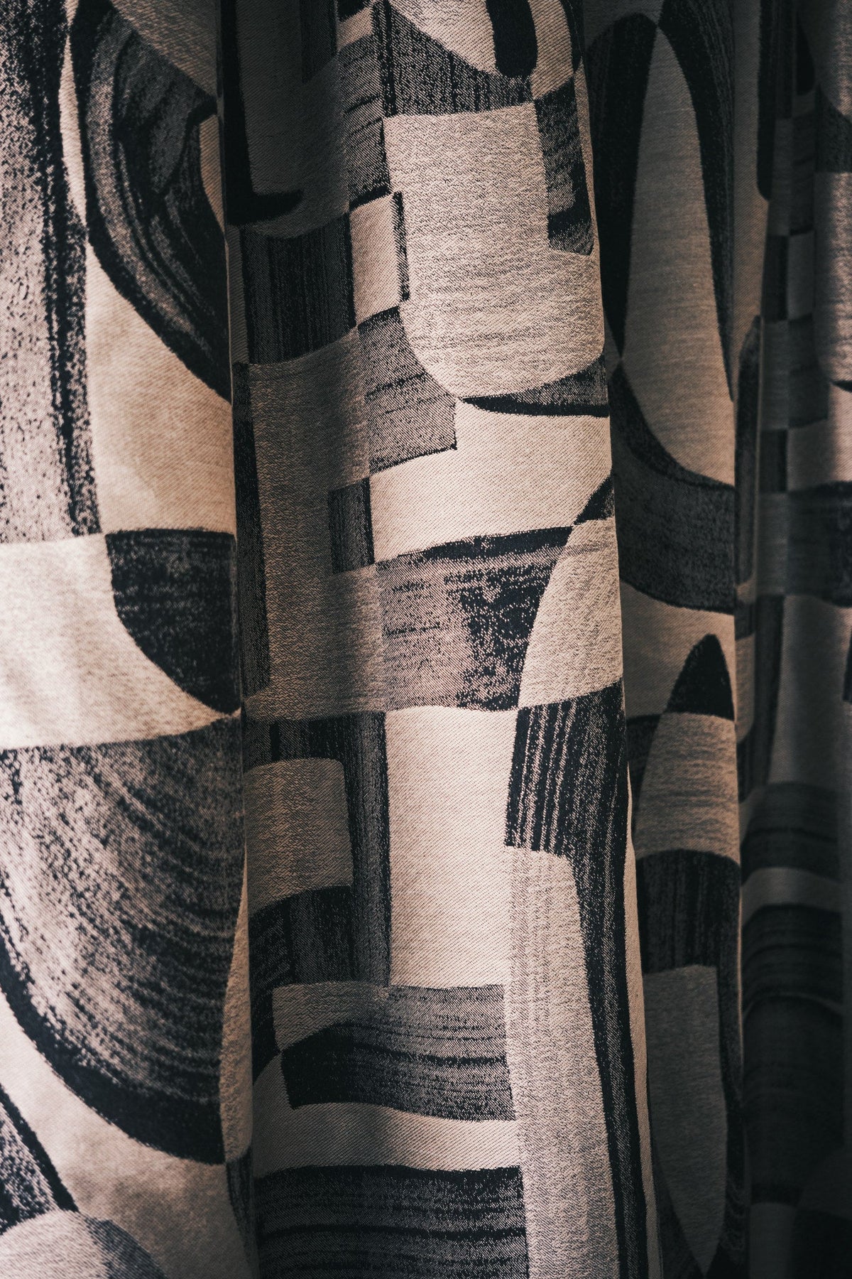 Black and tan abstract jacquard fabric hung as floor-length curtains falling in soft folds