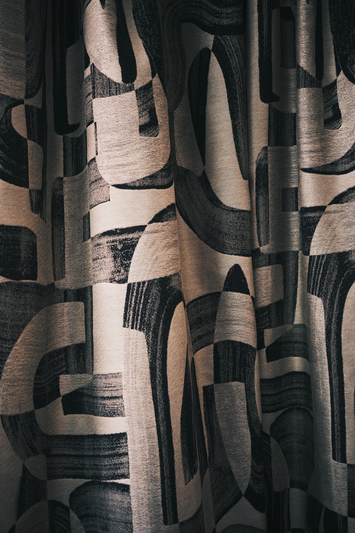 Black and tan abstract jacquard fabric hung as floor-length curtains shown close up in deep folds