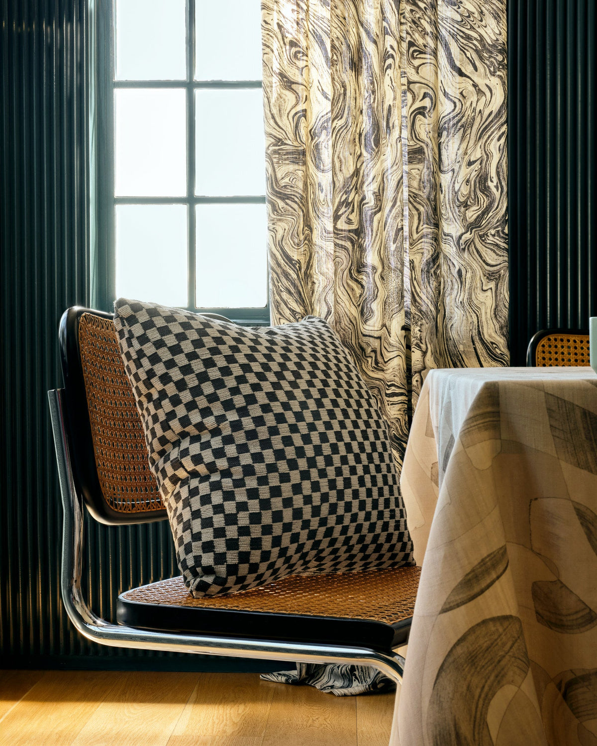 Black and cream checkerboard jacquard fabric made up as a throw pillow beside a cane dining chair in a panelled room