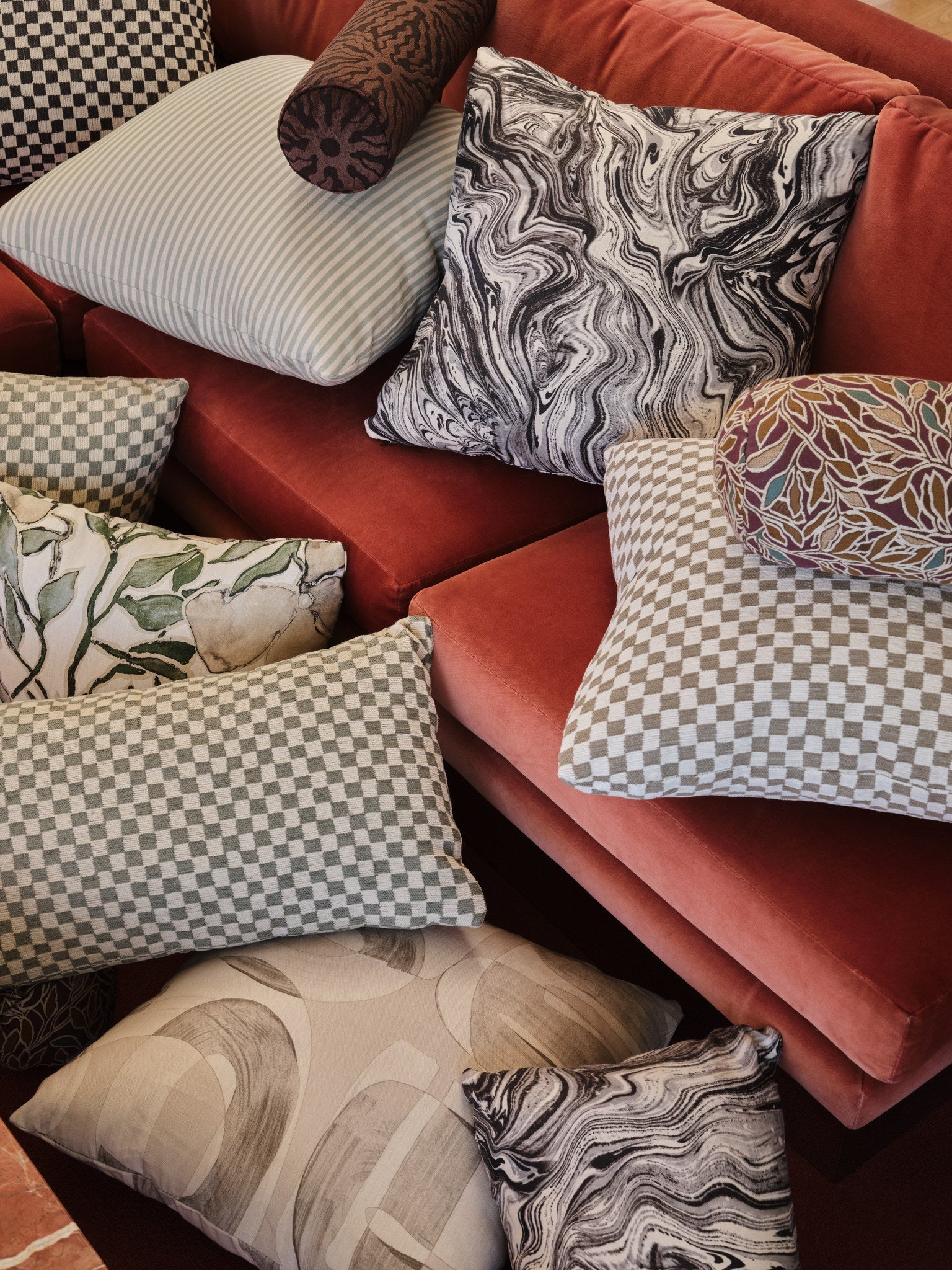 Gray checkerboard jacquard fabric made up as a throw pillow massed with other pillows on a velvet sofa