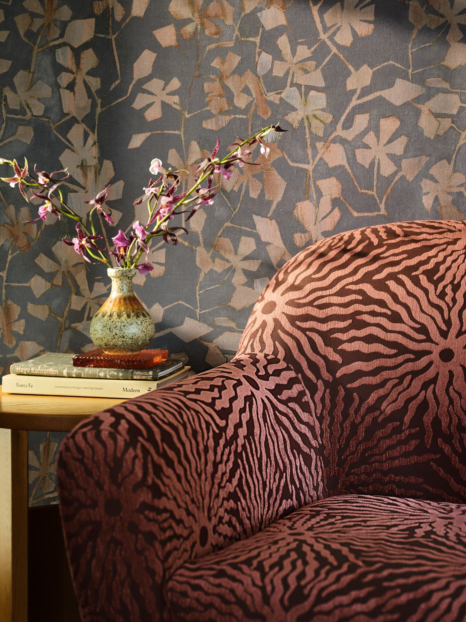 Blue floral cotton wallpaper hung on the wall shown close up on a sofa arm with orchids