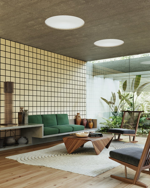 Contemporary living space featuring black and tan grid-patterned wallpaper, a floating concrete sofa with green cushions, wooden accent chairs, and large windows overlooking lush greenery, creating a serene and modern Japandi atmosphere.