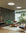 Contemporary living space featuring black and tan grid-patterned wallpaper, a floating concrete sofa with green cushions, wooden accent chairs, and large windows overlooking lush greenery, creating a serene and modern Japandi atmosphere.