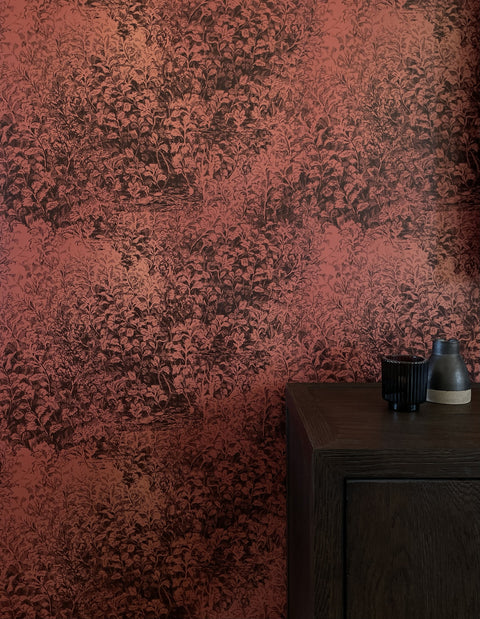 Dramatic botanical wallpaper in a deep rust-red hue with intricate foliage illustrations, styled with a dark wooden cabinet and minimalist decor.