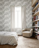 Cozy bedroom featuring a textured botanical wallpaper in white complemented by a neutral bedspread, cream-colored armchair, and built-in wooden bookshelves.