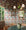 Dining room with multi-colored floral wallpaper covering walls and ceiling, featuring pink, green, and purple leaf patterns; green marble table, wicker chairs, and rustic chandelier with white shades in the foreground.