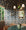 Dining room with blue floral wallpaper covering walls and ceiling, featuring blue leaf patterns; green marble table, wicker chairs, and rustic chandelier with white shades in the foreground.