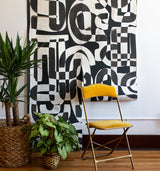 2 Drops of Down the Rabbit Hole Wallpaper on an office wall with yellow velvet folding chair and two house plants