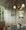 A dining room featuring wallpaper with a lush botanical pattern in green, pink, and blue tones, extending onto the ceiling. The space is decorated with a rope chandelier, wicker chairs, and a green marble table.