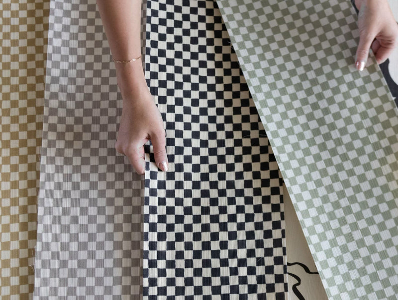 Printed checker board grasscloth wallpaper with woman's hand holding swatches of material