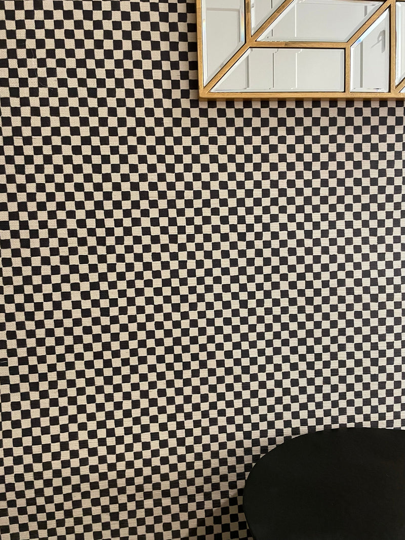 Black checkerboard patter on grasscloth wallpaper with gold mirror and black chair back