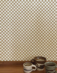 Taupe colored checker grasscloth wallpaper with 3 ceramic mugs on a wooden shelf in bottom of photo