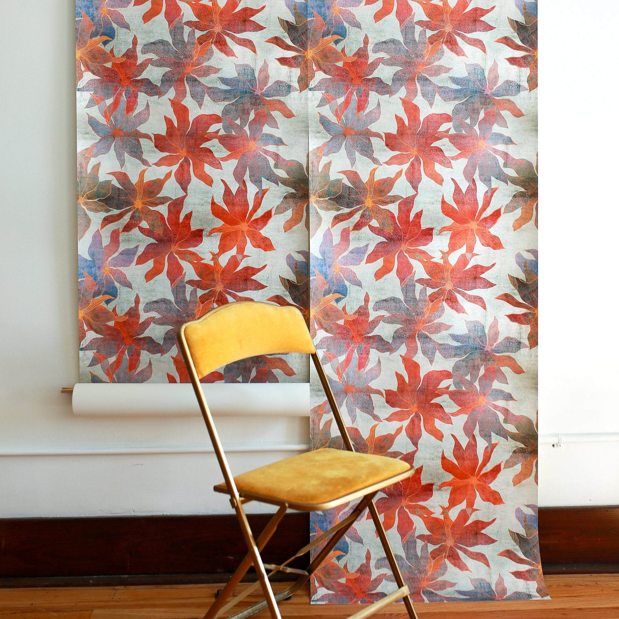 floral patterned wallpaper with red, orange and blue flowers, displayed in hanging panels; mustard-yellow folding chair placed in front for scale and contrast.